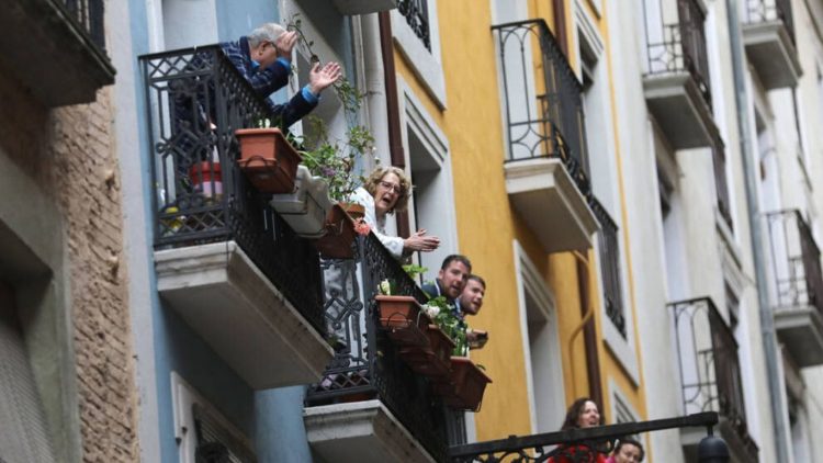 Un edificio con balcones, gente en ellos aplaudiendo.