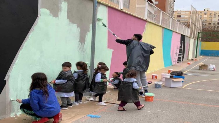 Niños del Colegio La Salle Montemolín pintando el mural solidario en el patio junto a uno de los voluntarios de Believe in Art